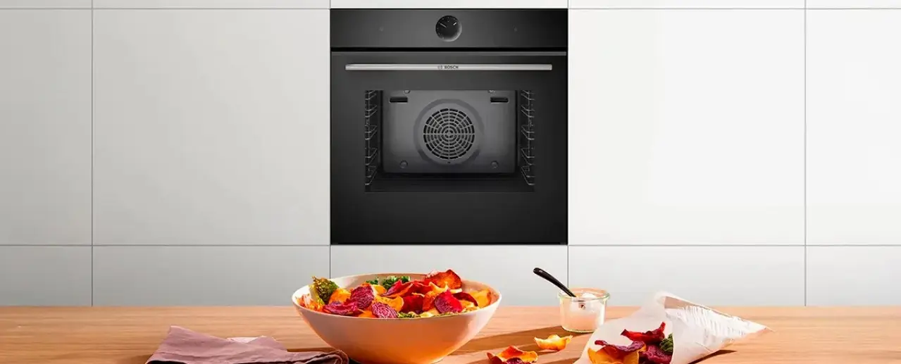 Zwarte Bosch inbouwoven met huisgemaakte groentechips op de voorgrond.