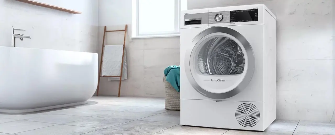 White Bosch dryer in a bathroom with a deep white bathtub and laundry basket.