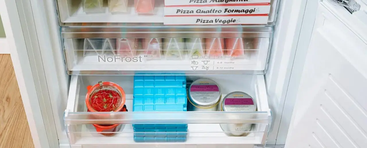 Vriezer met geopende deuren en 3 vrieslades gevuld met o.a. diepvriespizza's.