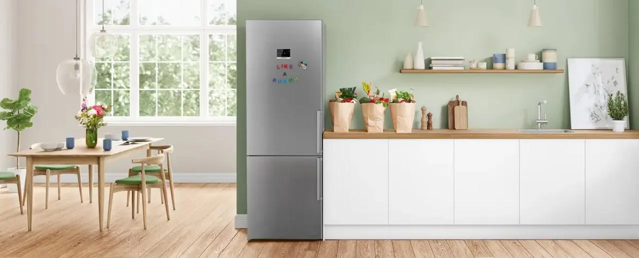 Vrijstaande RVS Bosch-koelkast in een lichte wit-houten keuken met planten en eethoek.