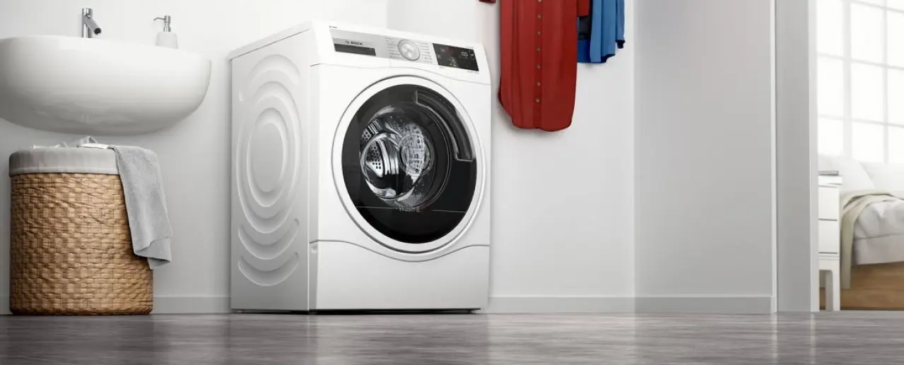 White Bosch washer next to a sink with a laundry basket underneath.