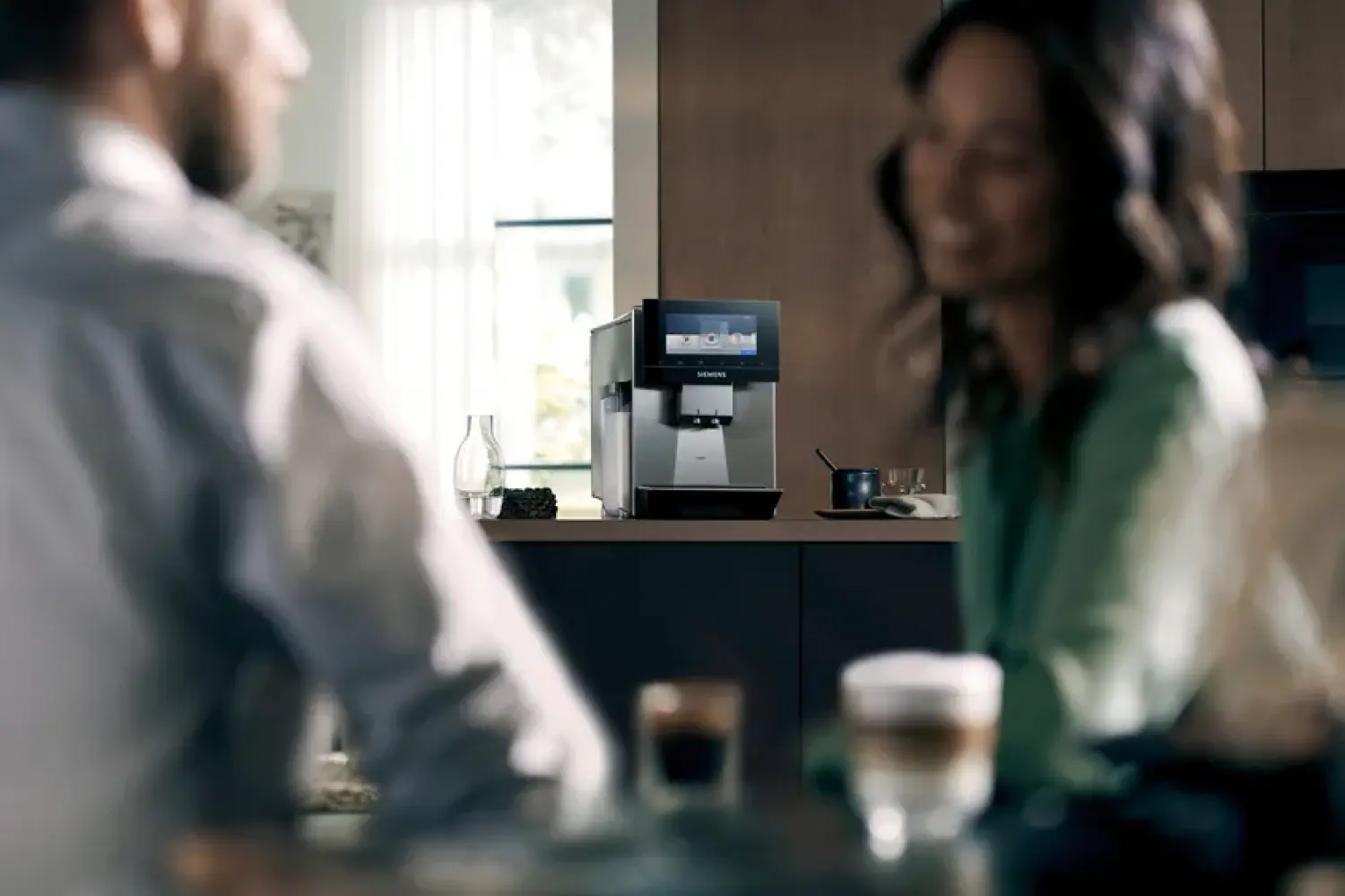 Man und Frau in einer Buerosituation trinken gemeinsam Kaffee. Im Hintergrund ein Kaffeevollautomat.