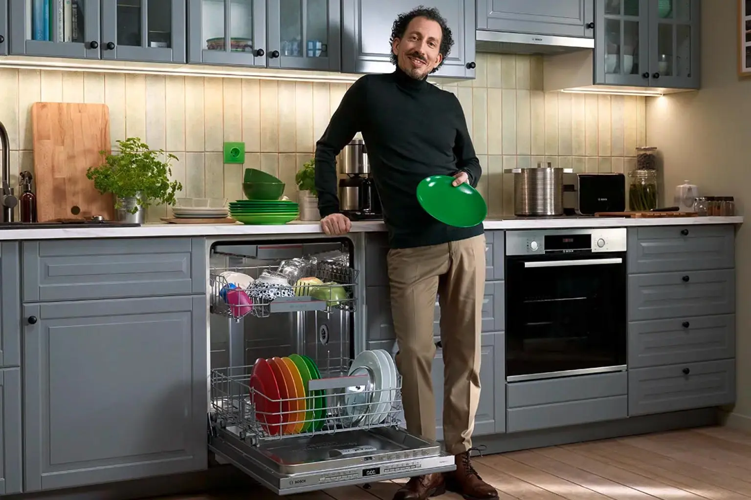 Ein Mann steht neben einem offenen Geschirrspüler und hält einen grünen Teller in der Hand.