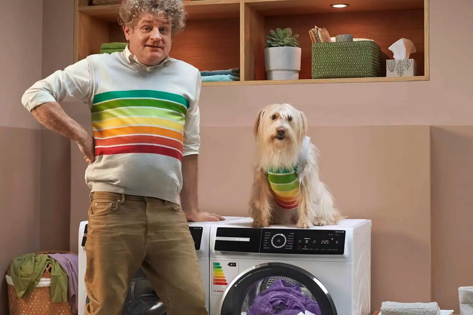 Man met energielabel trui staat naast wasmachine waarop een hond zit met dezelfde trui.