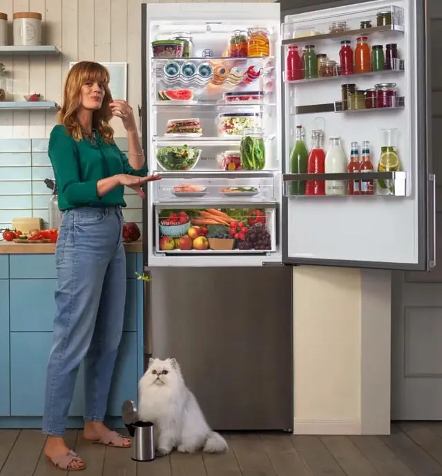 Vrouw naast open Bosch koelkast met witte kat op de grond.