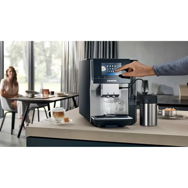 Maennerhand beruehrt Display von Kaffeevollautomat. Automat steht auf Spuele. Im Hintergrund Frau an einem Tisch.