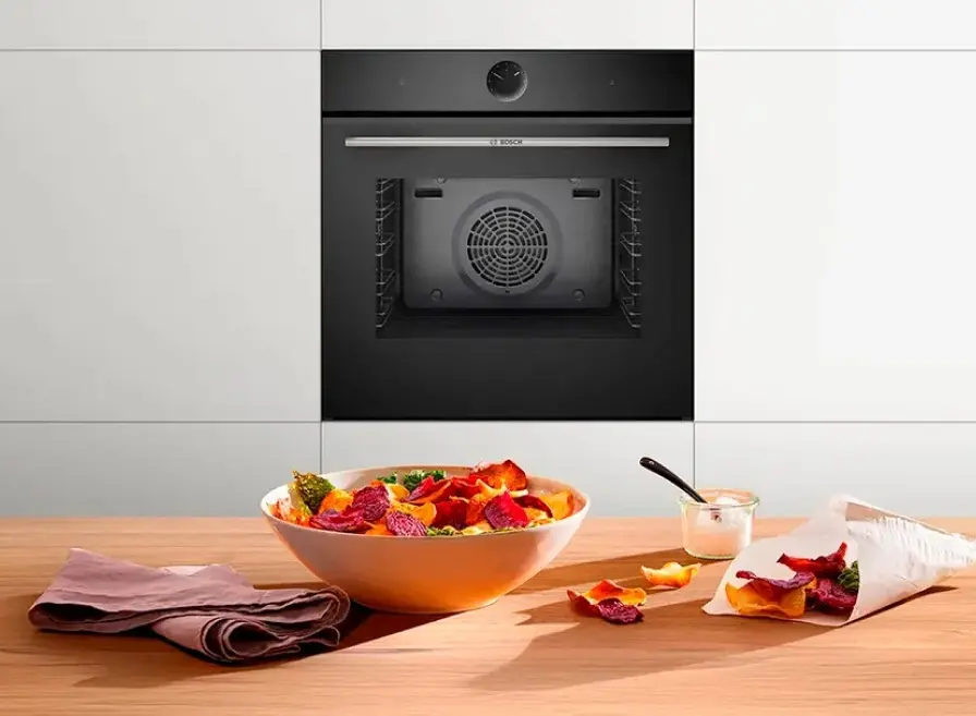 Zwarte Bosch inbouwoven met huisgemaakte groentechips op de voorgrond.