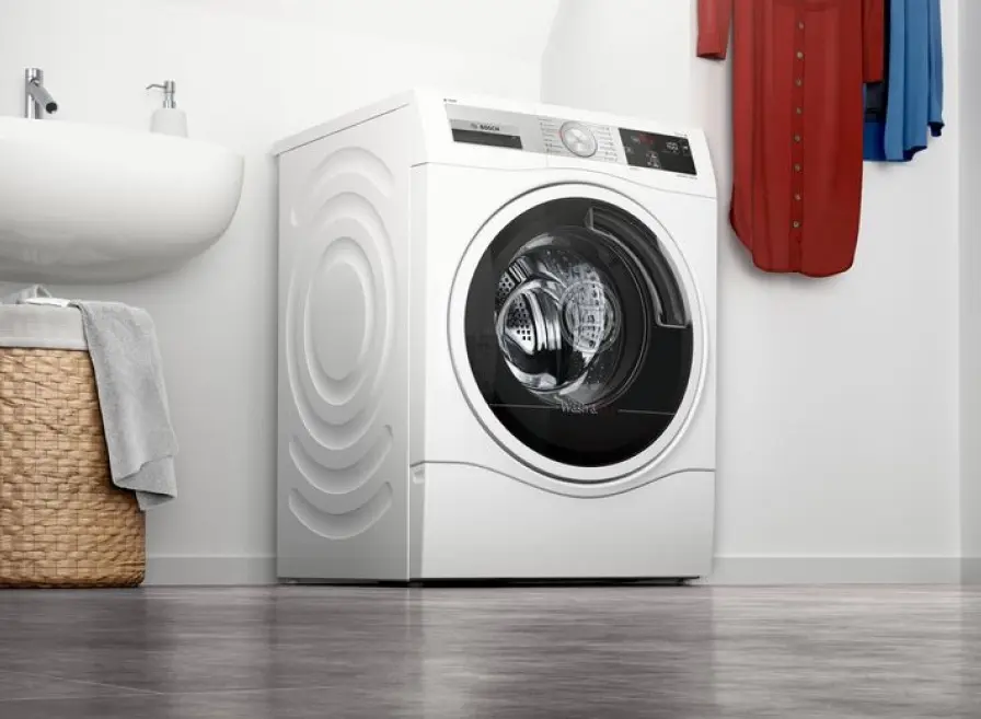 White Bosch washer next to a sink with a laundry basket underneath.