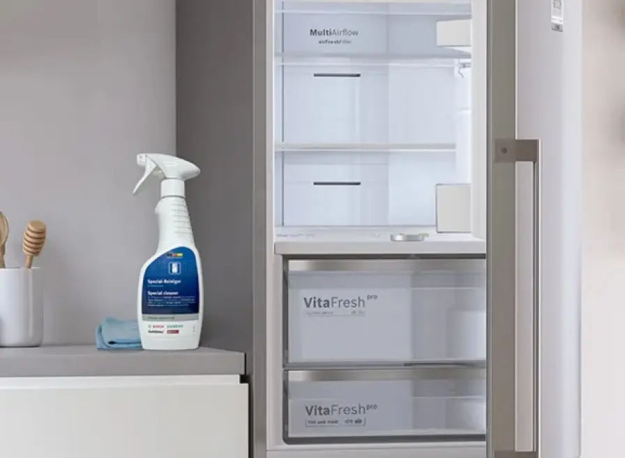 Empty Bosch refrigerator with the door open and cleaning supplies next to it on the counter.