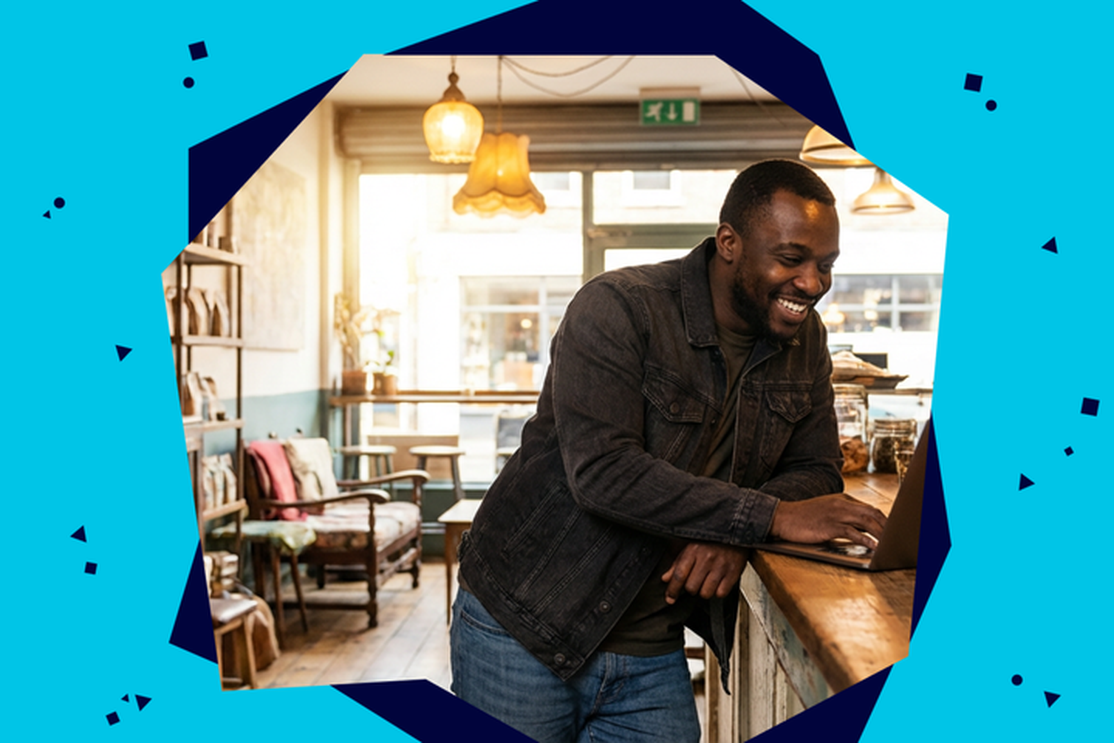 Man smiling while using a laptop at a cozy cafe counter, with warm lighting and a relaxed atmosphere.