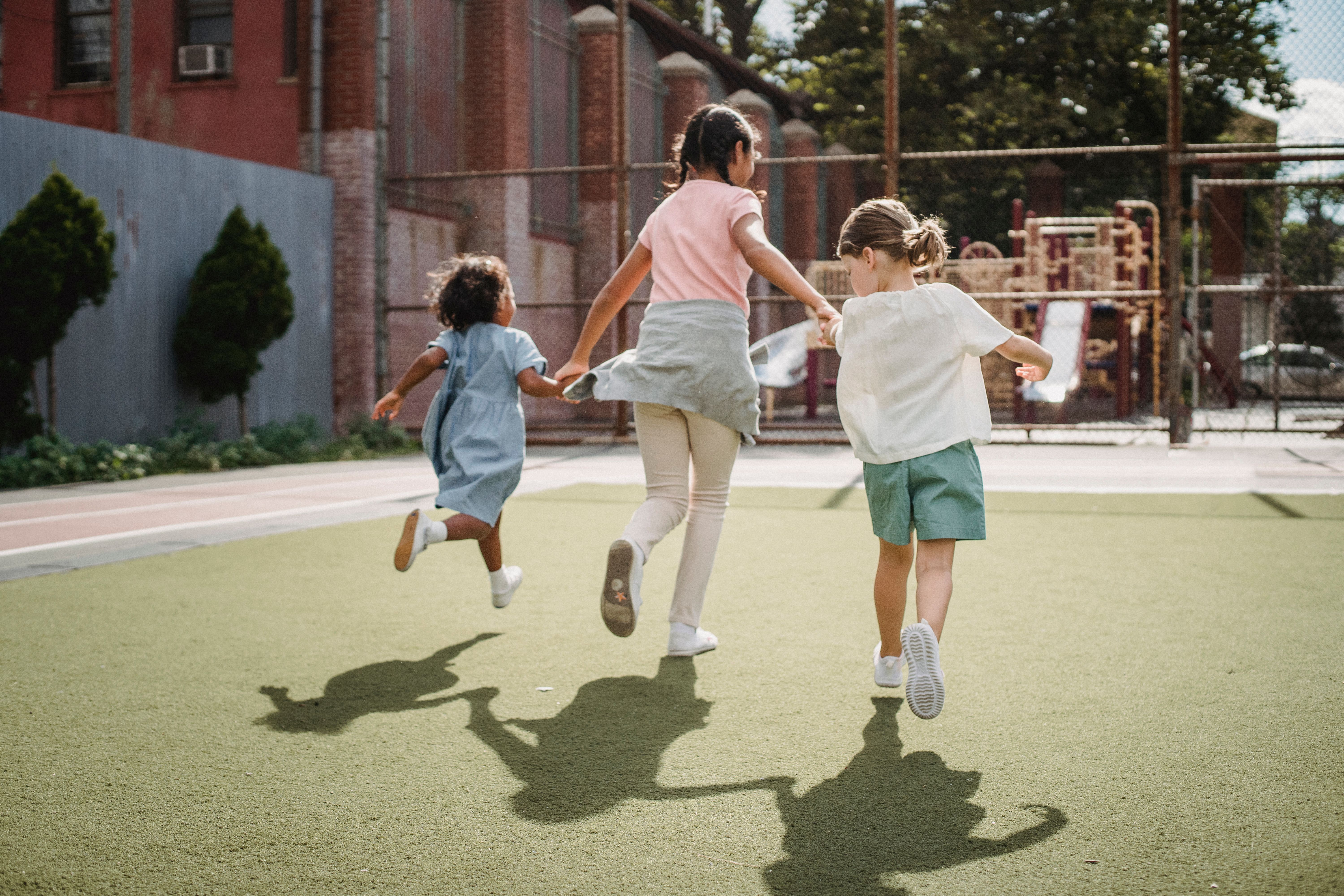 3 kinderen houden elkaars hand vast en spelen buiten
