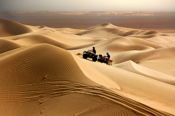 Twee mensen rijden met quads over stevige zandduinen in de woestijn onder een heldere lucht.