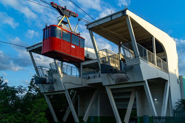Rode kabelbaan die een modern station verlaat, tegen een achtergrond van bomen en een gedeeltelijk bewolkte lucht.