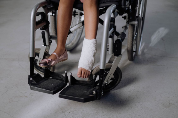 Persoon in een rolstoel met één been in het gips en roze schoenen, met de rolstoel op een gladde ondergrond.