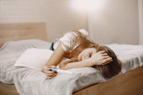 Een vrouw ligt op een bed en kijkt nadenkend naar een zwangerschapstest, bij zacht licht in een gezellige slaapkamer.