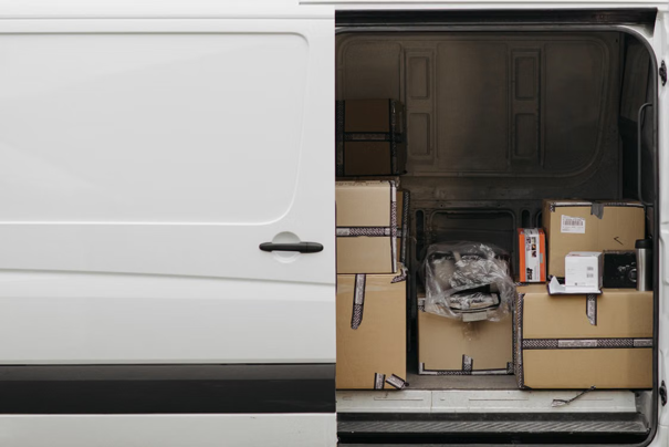 Bestelwagen met open schuifdeur, waarin gestapelde kartonnen dozen en pakketten zichtbaar zijn.