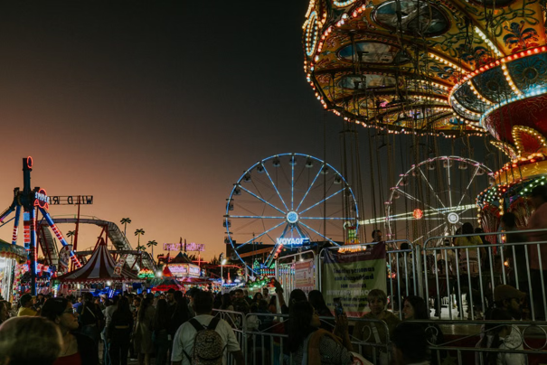 Een drukbezochte kermis bij zonsondergang met verlichte attracties, waaronder een reuzenrad en zweefmolen.