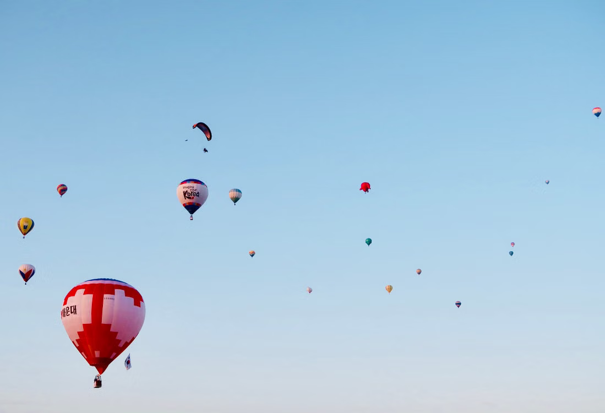 Kleurrijke heteluchtballonnen zweven in een helderblauwe lucht, met op de voorgrond één opvallende rood-witte ballon.