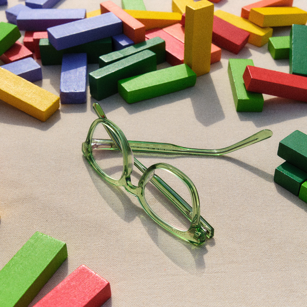 Grüne Kinderbrille liegt auf einem Tisch zwischen bunten Holzbausteinen.