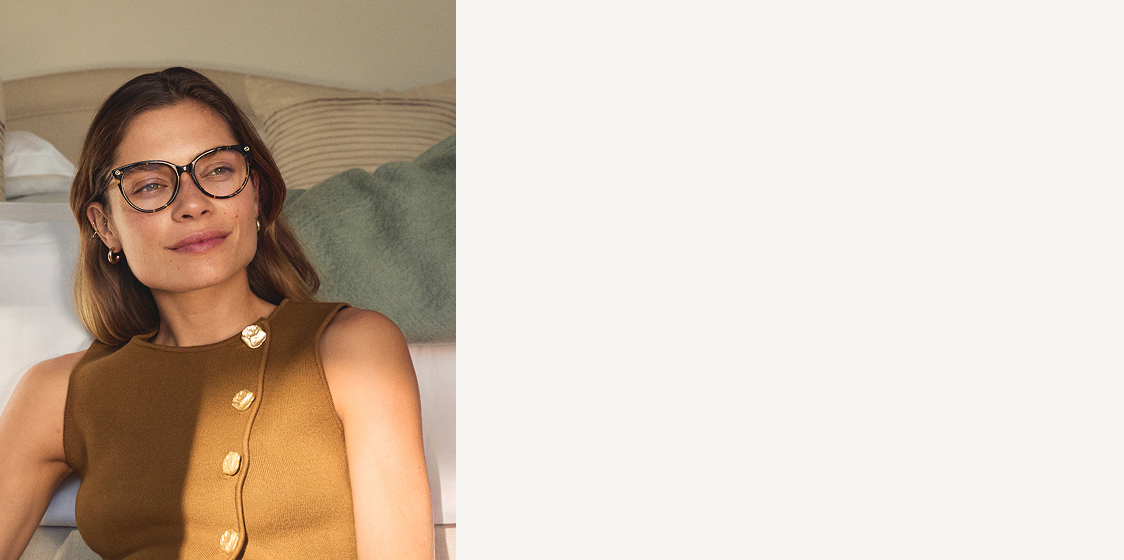 Una donna con occhiali e una maglia marrone è seduta davanti a un letto.