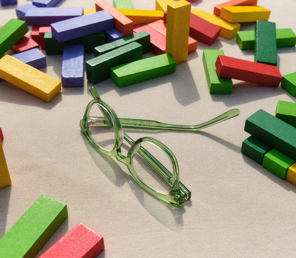 Grüne Kinderbrille liegt auf einem Tisch zwischen bunten Holzbausteinen.