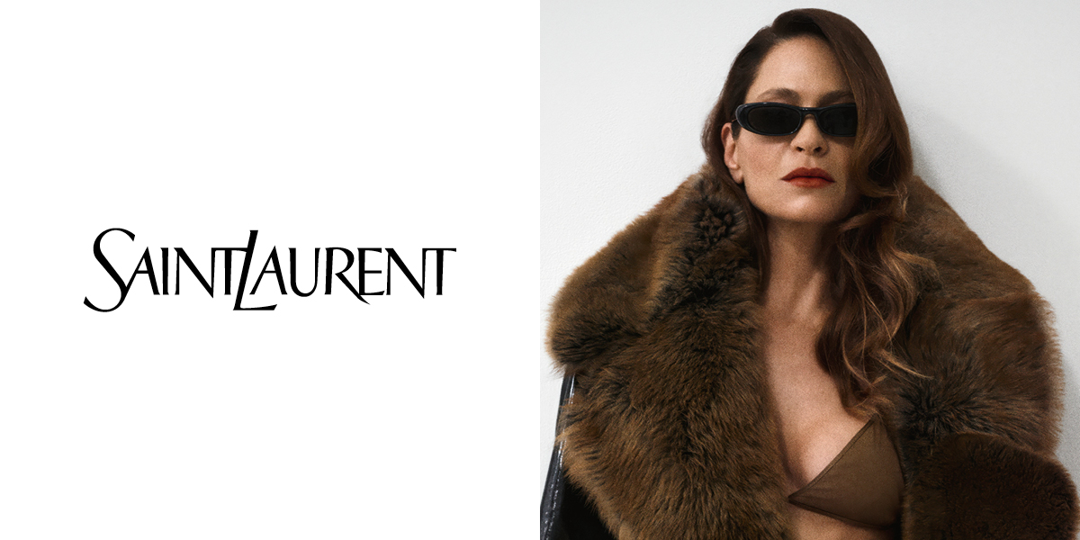 È visibile il logo Saint Laurent. Una donna con i capelli lunghi, occhiali da sole e un cappotto con collo di pelliccia, che posa su uno sfondo bianco.