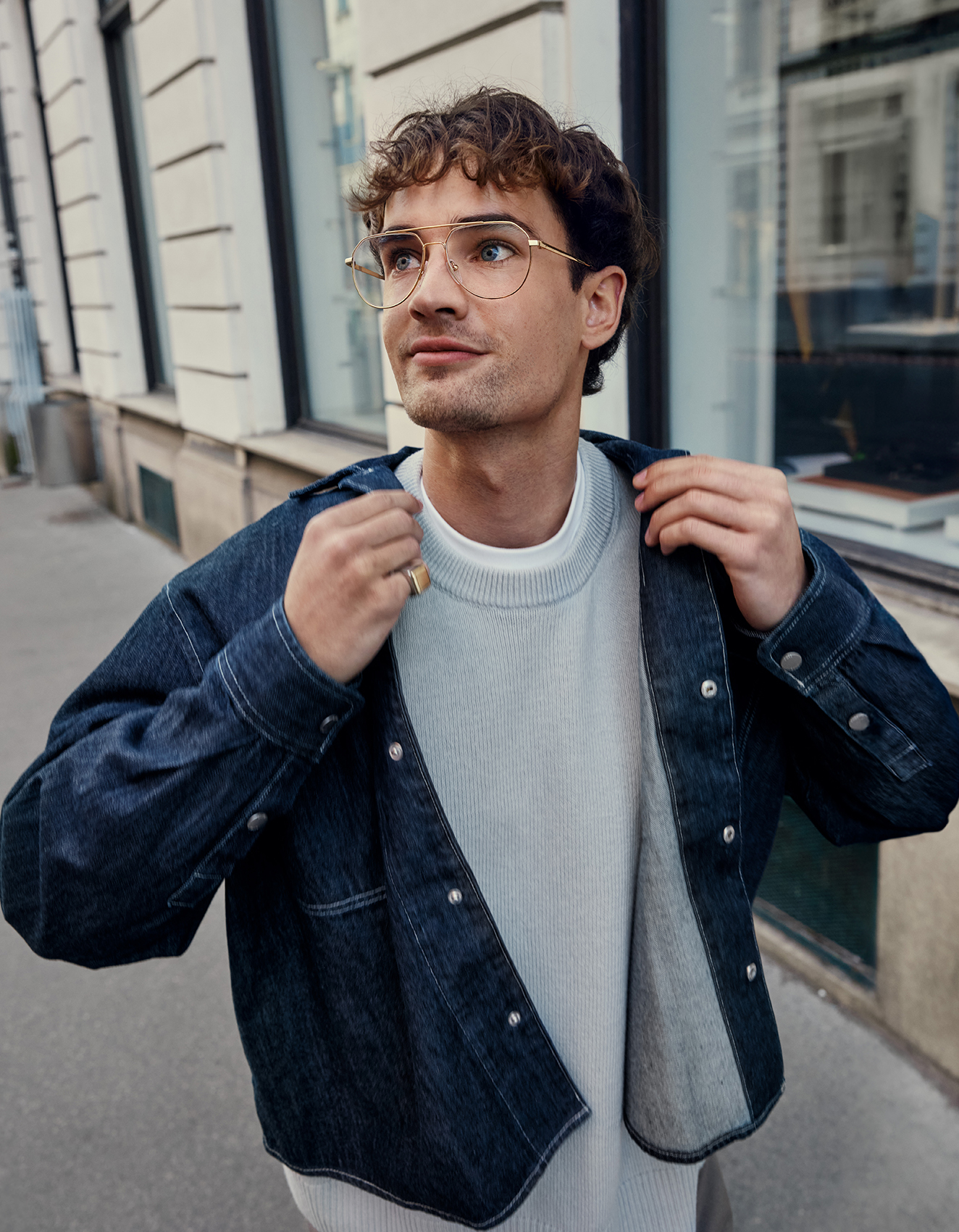 Junger Mann mit einer Brille in Aviator-Form steht vor einem Gebäude.
