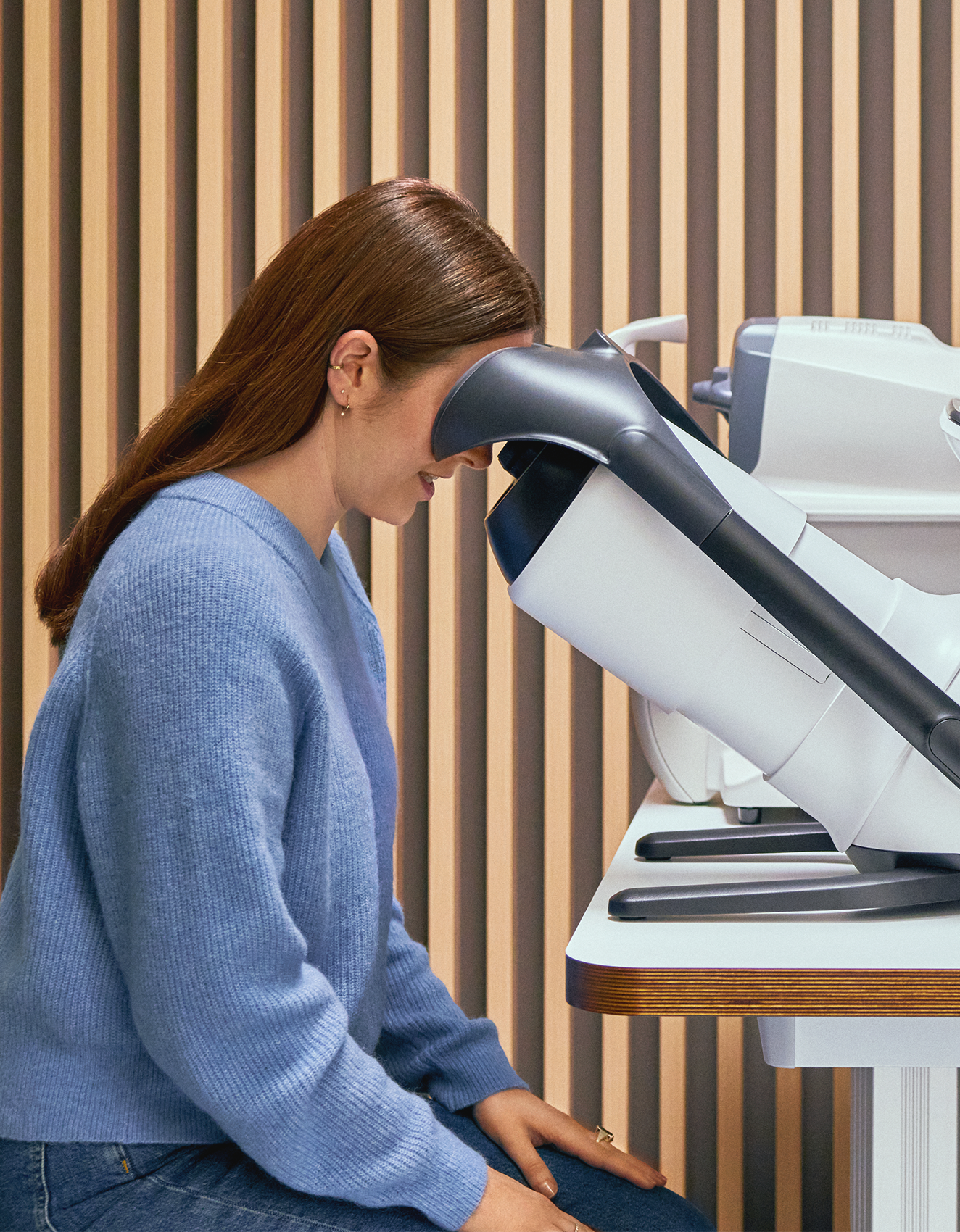 Eine Frau in einem blauen Pullover unterzieht sich einer Augenuntersuchung mit einem modernen Gerät bei einem Optiker.