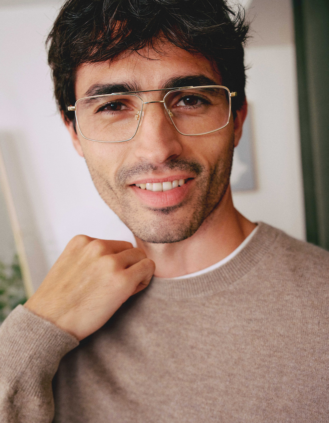 Un uomo con gli occhiali e un maglione marrone, che sorride con sicurezza e tiene una mano appoggiata con disinvoltura sulla nuca.