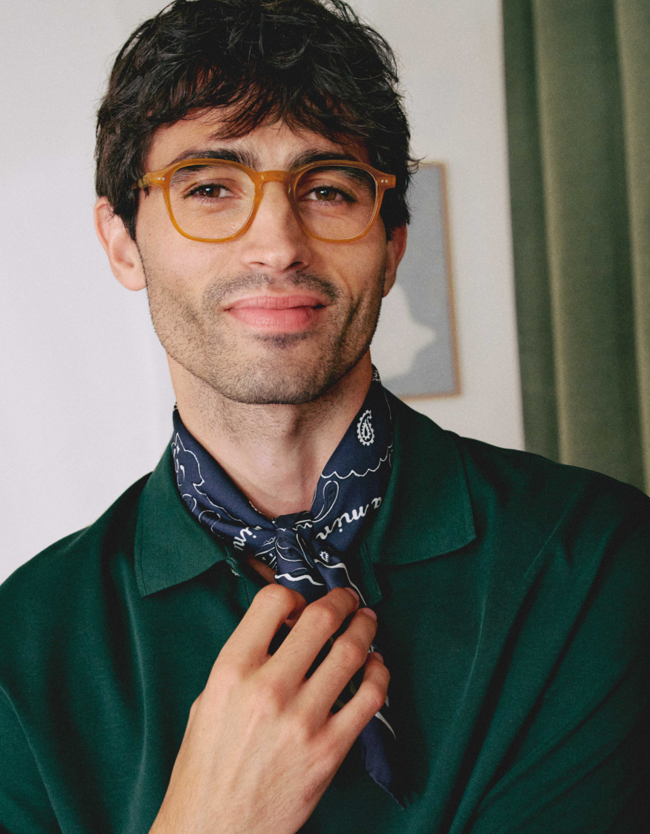 Ein Mann mit kurzen dunklen Haaren, der eine braune Brille, ein dunkelgrünes Hemd und einen gemusterten Schal um den Hals trägt, lächelt in die Kamera.