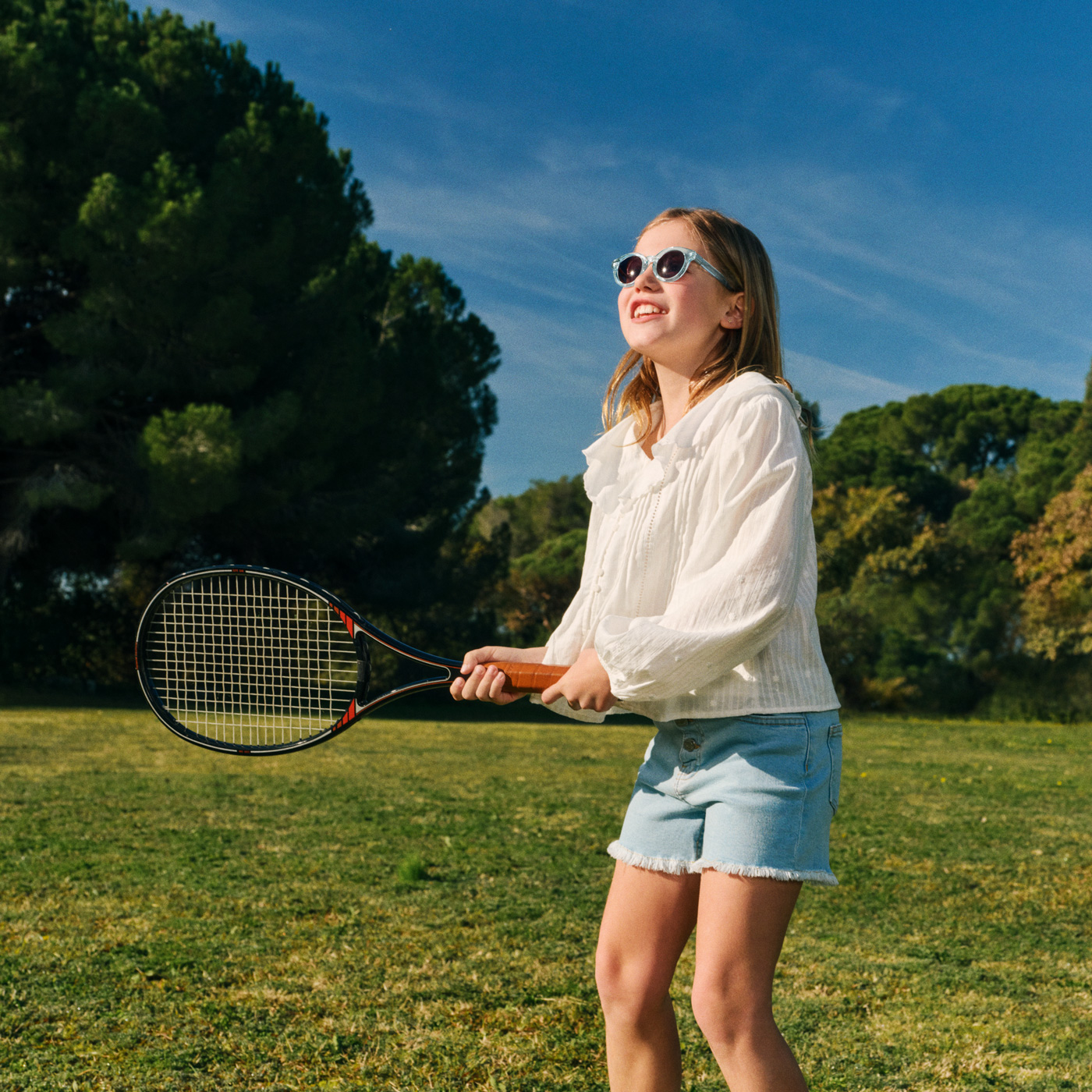 Mädchen mit Sonnenbrille spielt Tennis auf dem Rasen.
