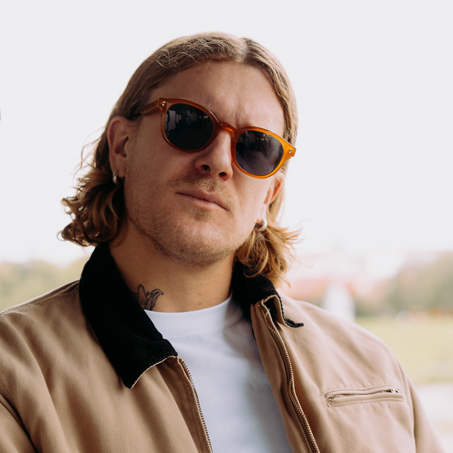 L’artiste Peter-Maximilian Ronsdorf, portant des lunettes de soleil et une veste beige sur une chemise blanche, se tient à l’extérieur.