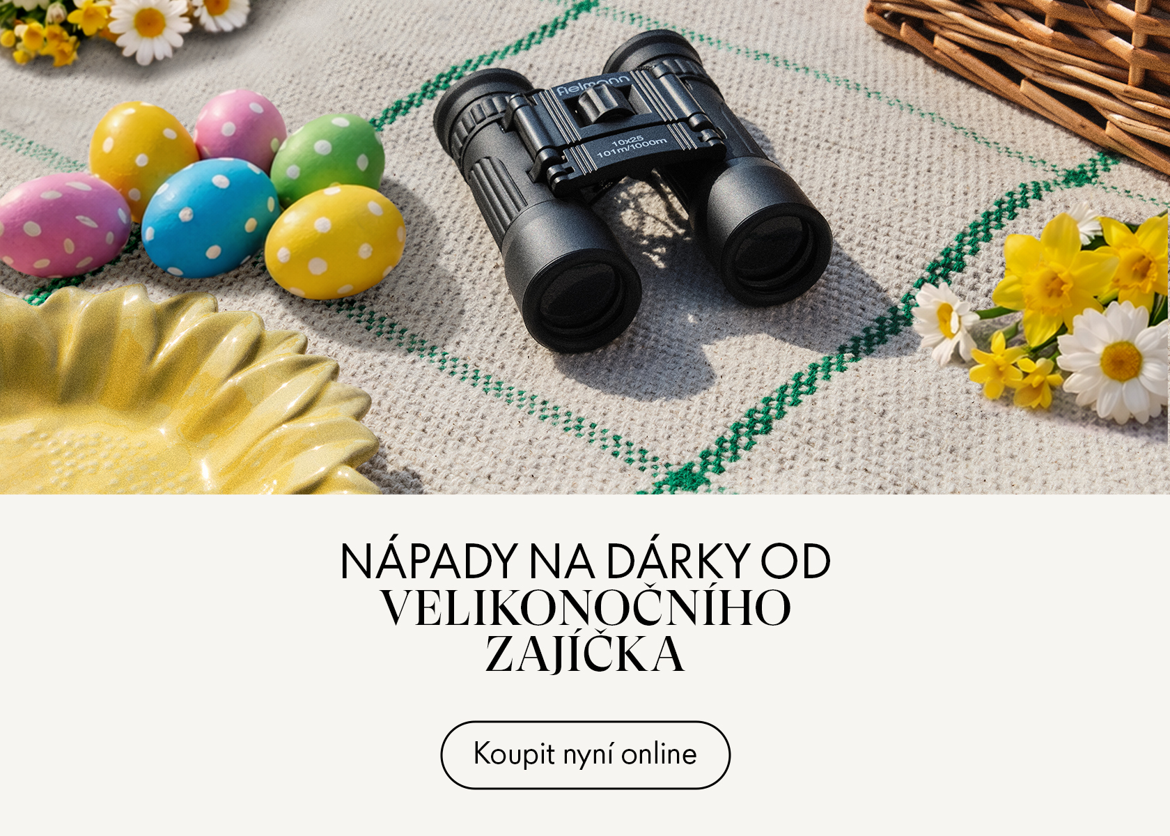 Dalekohled na piknikové dece s barevnými velikonočními vajíčky, sedmikráskami a košíkem.