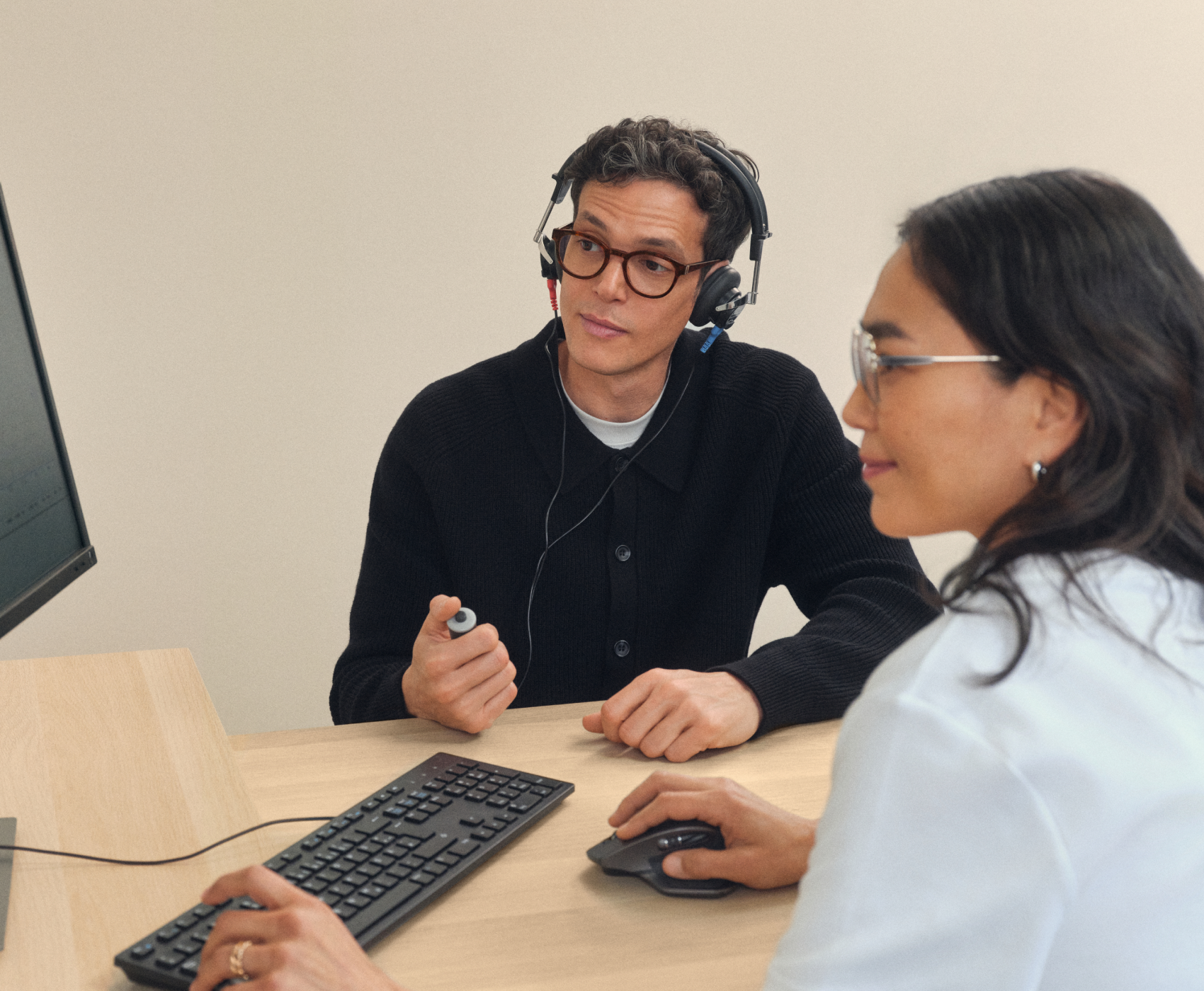 Deux personnes sont assises à un bureau, l’une porte un casque et regarde un écran d’ordinateur affichant des graphiques.