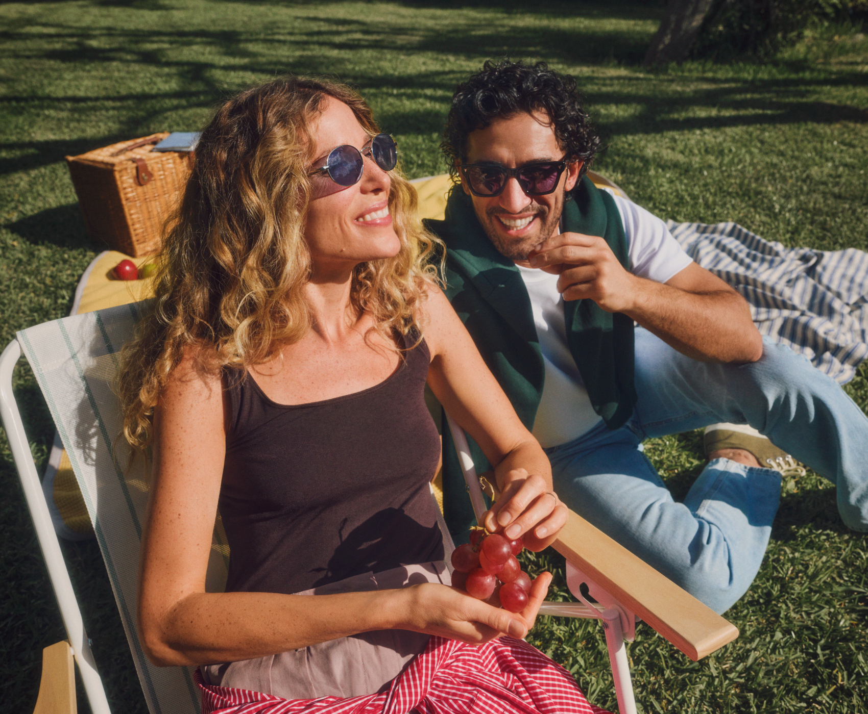 Eine Frau und ein Mann genießen ein Picknick auf dem Rasen. Sie lächeln und neben ihnen steht ein Korb. Die untere Hälfte des Bildes ist mit einem orangefarbenen Farbverlauf überzogen.