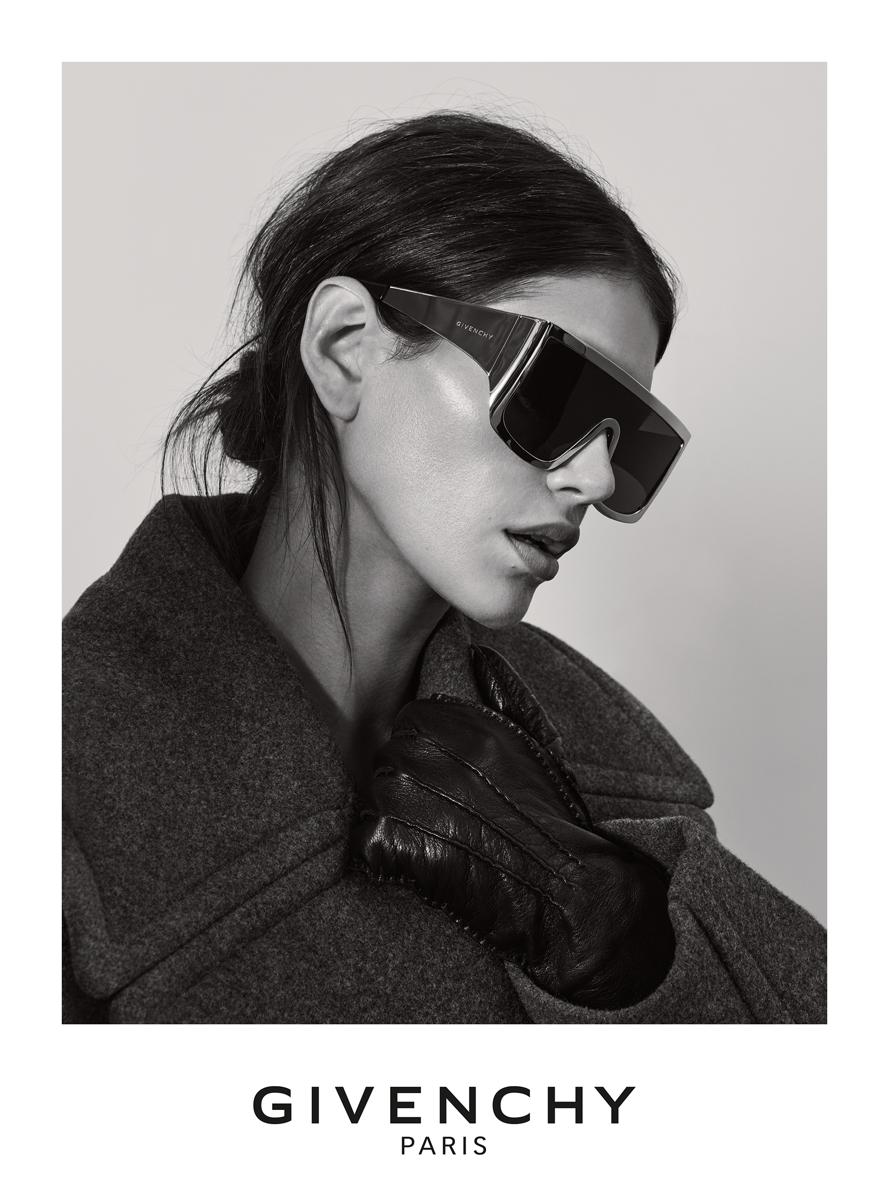 Frau mit dunklen Haaren in einer schwarzen Jacke und mit schwarzen Handschuhen. Sie trägt eine oversized Sonnenbrille von Givenchy.