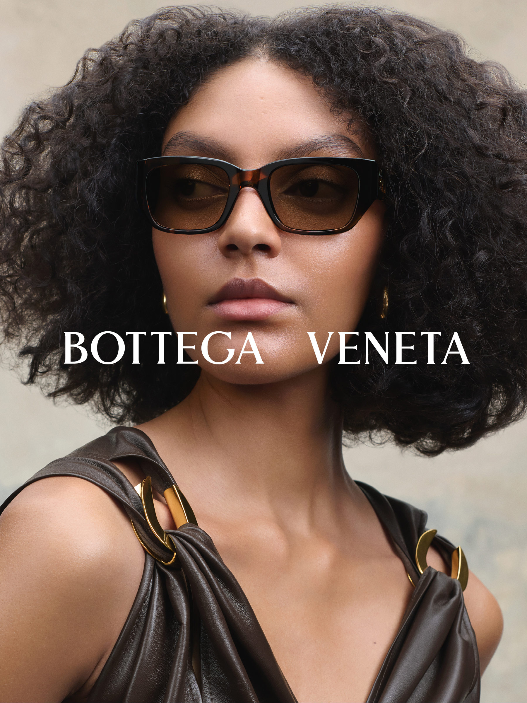 Osoba o kręconych włosach, nosząca okulary przeciwsłoneczne, z napisem „Bottega Veneta” nad nimi.