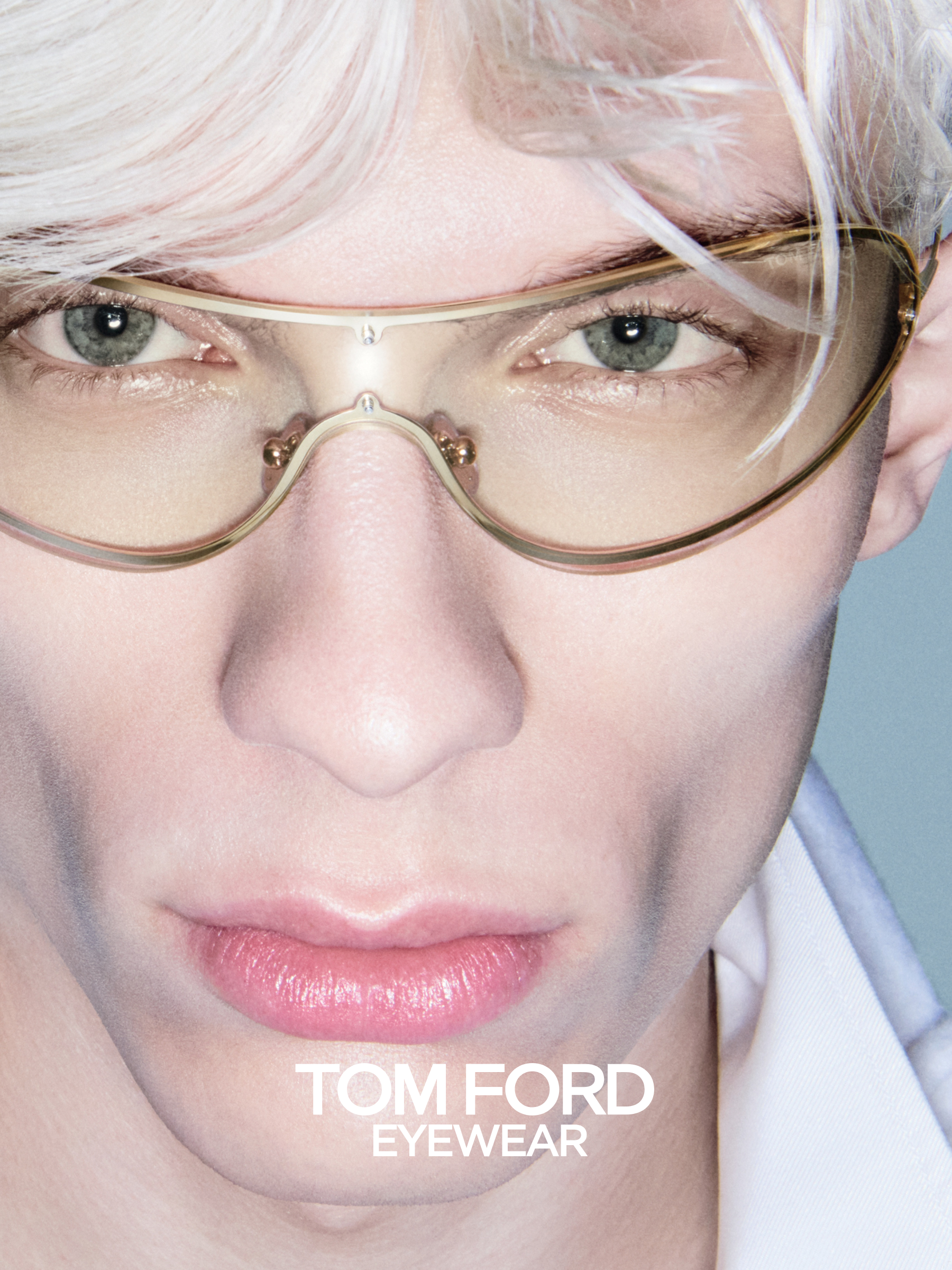 Detailní záběr osoby nosící brýle s čirými obroučkami s nápisem „TOM FORD EYEWEAR”. Jasné osvětlení zdůrazňuje rysy obličeje.