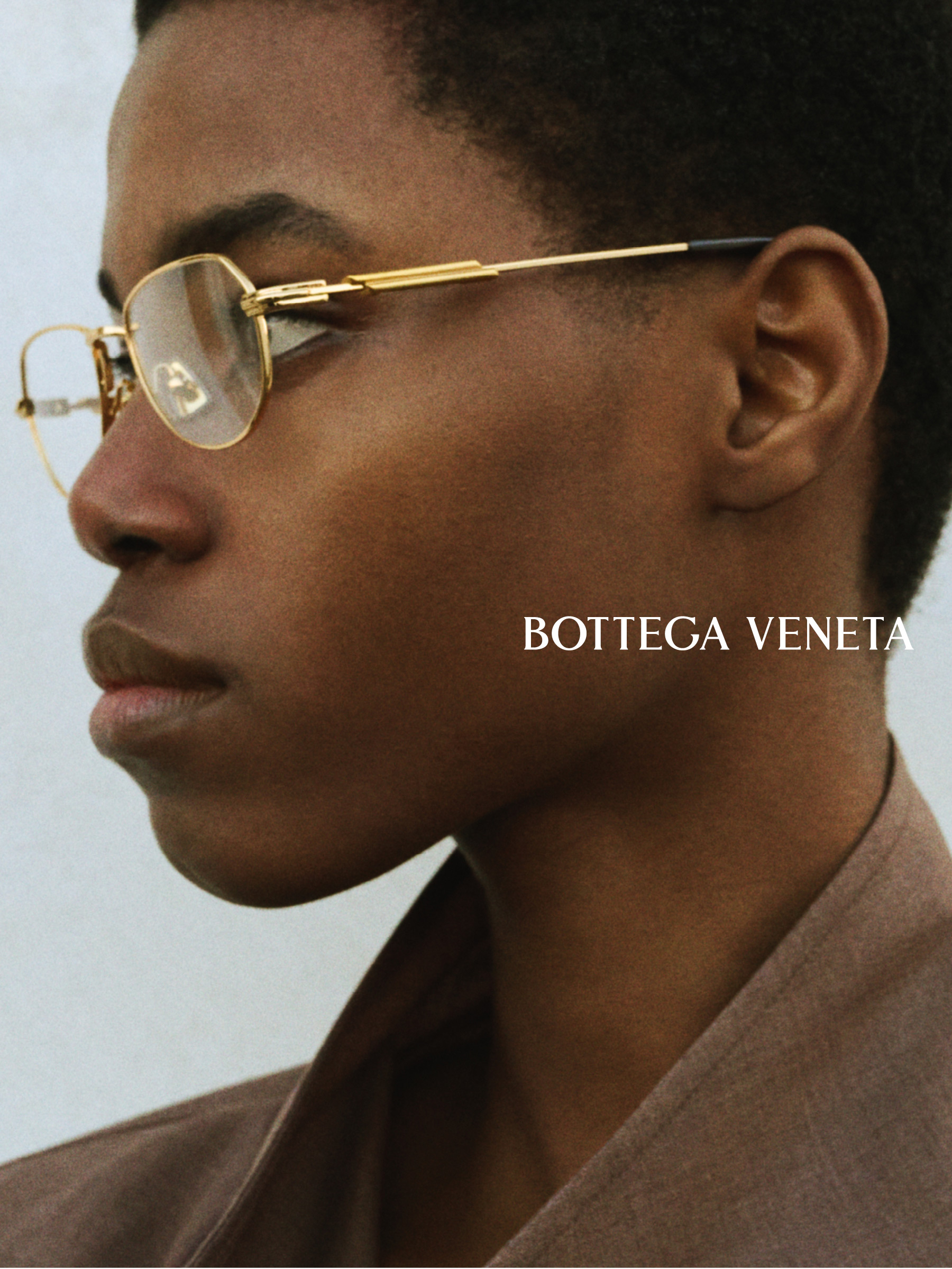Une personne portant des lunettes à monture dorée, avec l'inscription « Bottega Veneta » à côté, devant un fond uni.