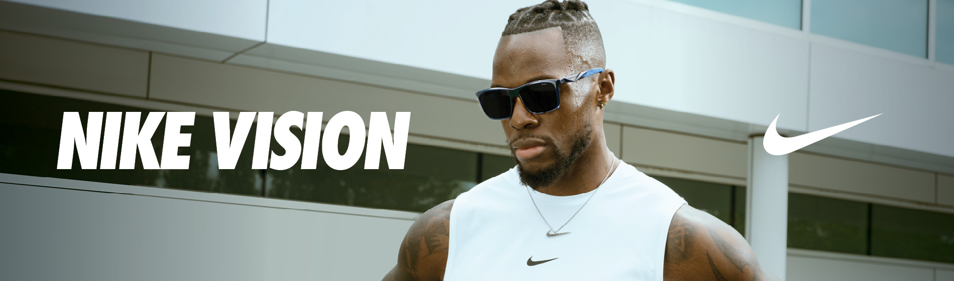 Mężczyzna w okularach przeciwsłonecznych i białej koszulce bez rękawów marki Nike stoi pewnie na świeżym powietrzu. Napis brzmi „Nike Vision”, a logo Nike jest widoczne.