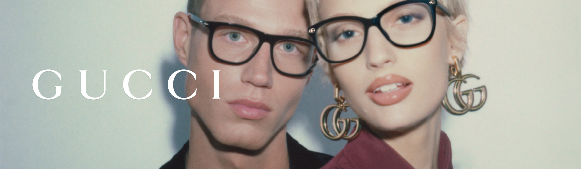 Dwie modelki w okularach, obok nich logo Gucci. Kobieta nosi duże kolczyki „GG”.