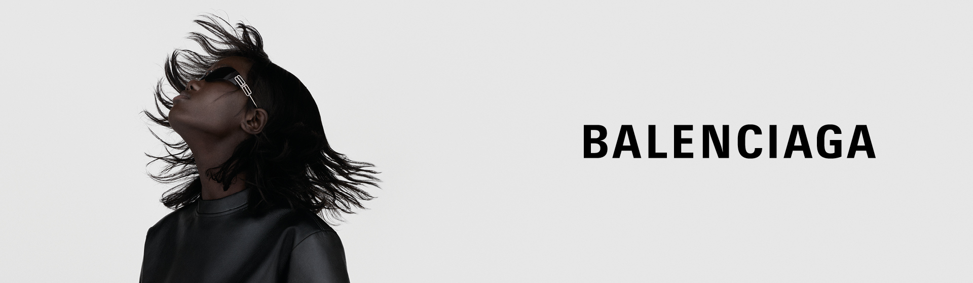 Osoba v černém koženém oblečení a slunečních brýlích naklání hlavu dozadu, přičemž jí splývají vlasy, nad obrázkem je nápis „BALENCIAGA”.