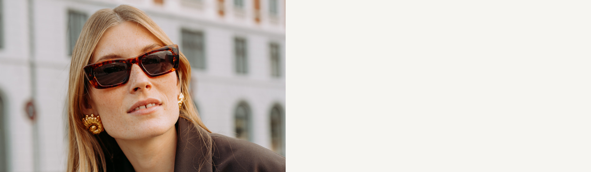 Nahaufnahme einer Frau mit langen blonden Haaren, die eine Schildpatt-Sonnenbrille, goldene Muschelohrringe und einen dunklen Blazer trägt.
