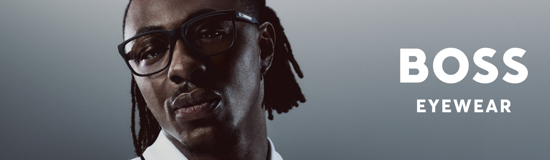 Eine Person mit Brille, auf deren rechten Seitensteg der Schriftzug „BOSS EYEWEAR“ zu sehen ist, vor einem Hintergrund mit Farbverlauf.