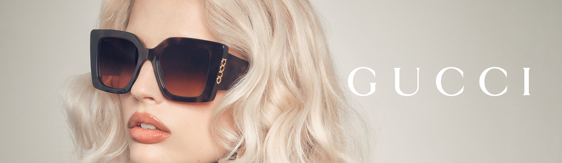 Osoba s blond vlasy, která nosí nadměrně velké sluneční brýle s nápisem „GUCCI”.