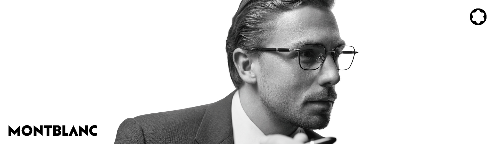 Mężczyzna w okularach i garniturze wygląda na zamyślonego na białym tle z logo „MONTBLANC” i emblematem.
