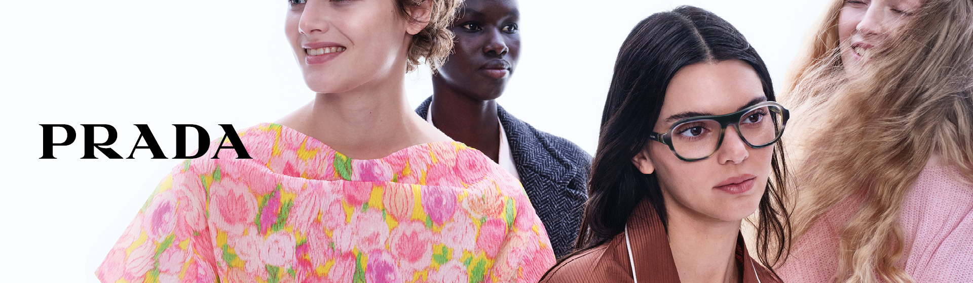 Un gruppo di persone vestite in modo colorato e alla moda posa insieme. Una persona indossa occhiali grandi. Nell'angolo in basso si vede la scritta “PRADA”.