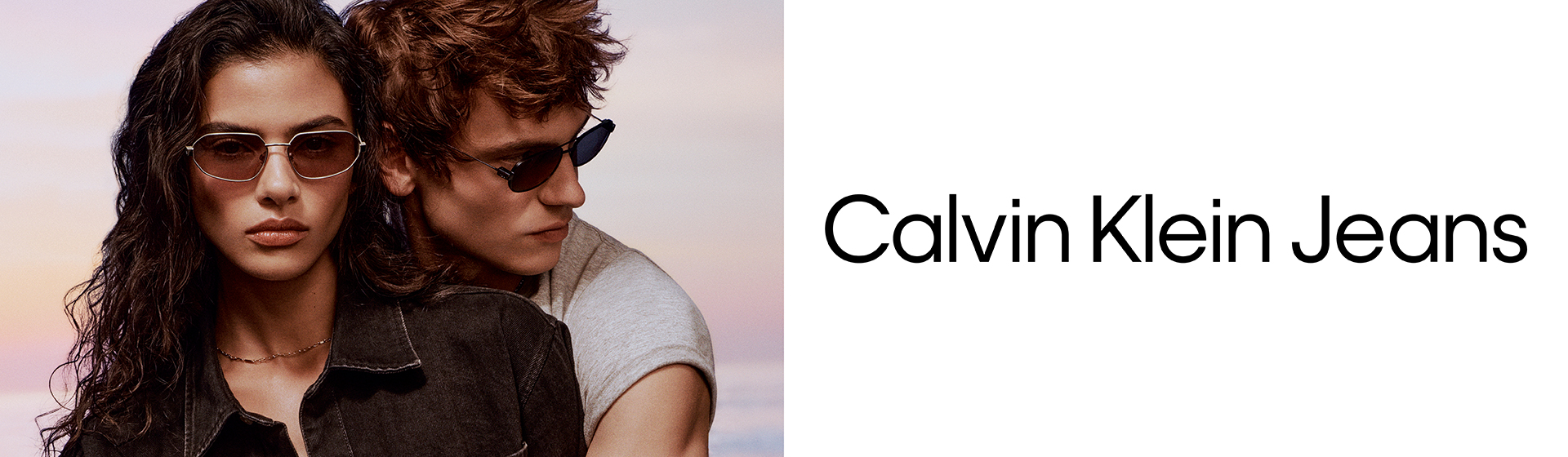 Deux mannequins portant des lunettes de soleil et des vêtements décontractés Calvin Klein, debout côte à côte devant un arrière-plan flou.