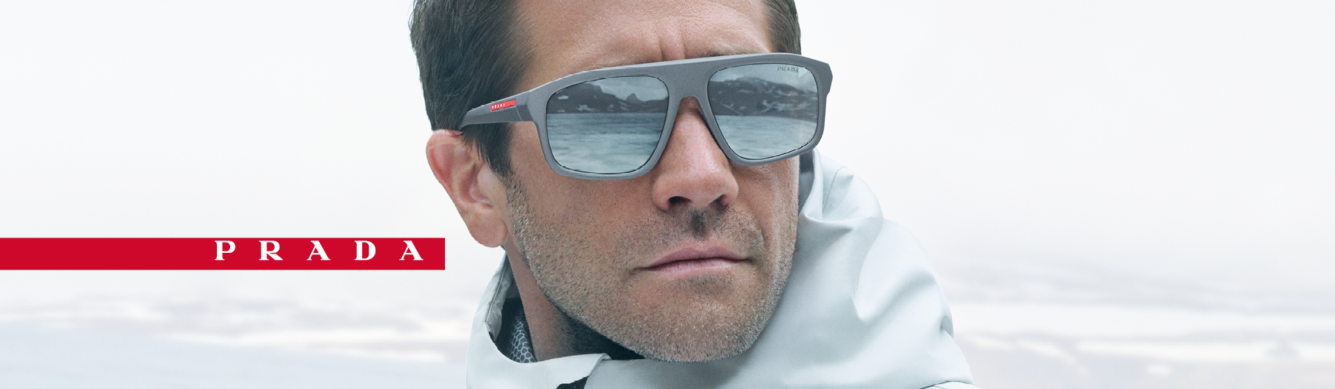 Homme portant des lunettes de soleil grises et une veste blanche avec un logo Prada.