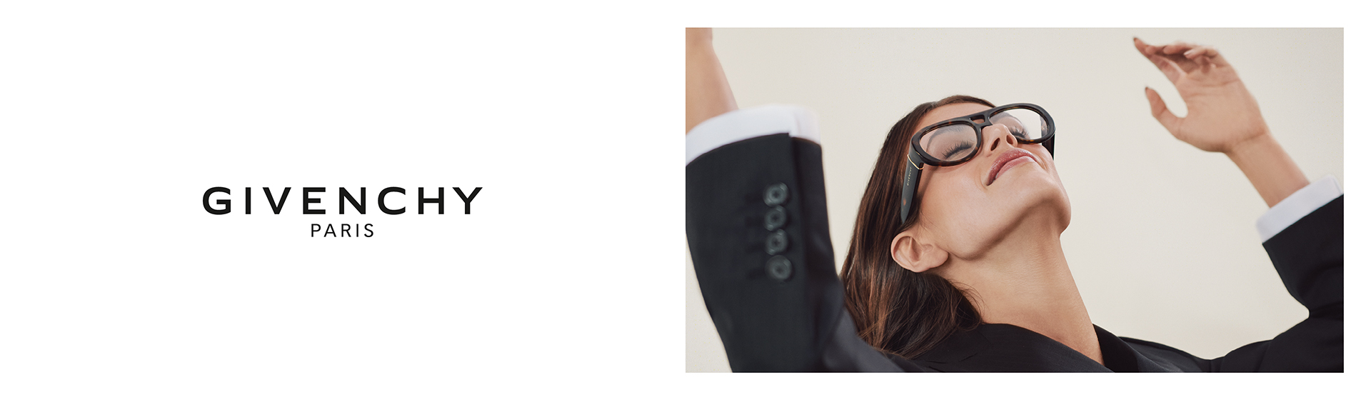 Eine Person in einem schwarzen Zweireiheranzug und Brille posiert mit erhobenen Armen vor einem einfarbigen Hintergrund. Givenchy-Logo seitlich.